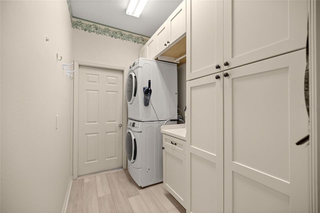 clothes washing area with stacked washing maching and dryer, cabinets, and light hardwood / wood-style flooring