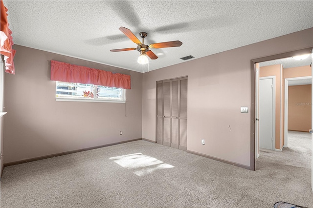 unfurnished bedroom featuring ceiling fan, light colored carpet, a textured ceiling, and a closet