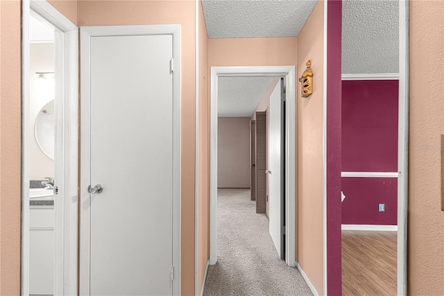 hallway with light colored carpet, sink, and a textured ceiling