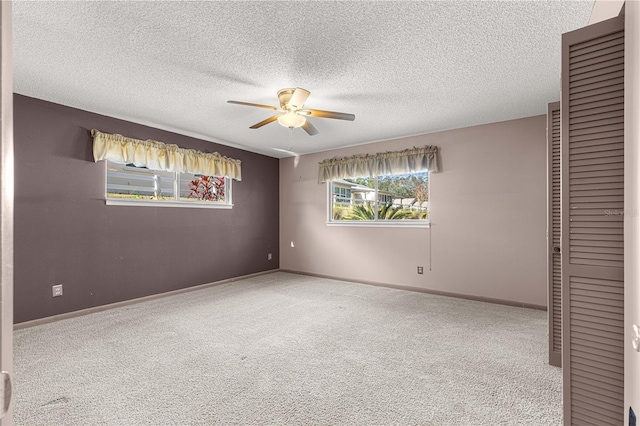 carpeted spare room with ceiling fan, plenty of natural light, and a textured ceiling