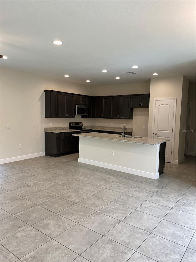 kitchen featuring light stone counters, stainless steel appliances, visible vents, baseboards, and an island with sink