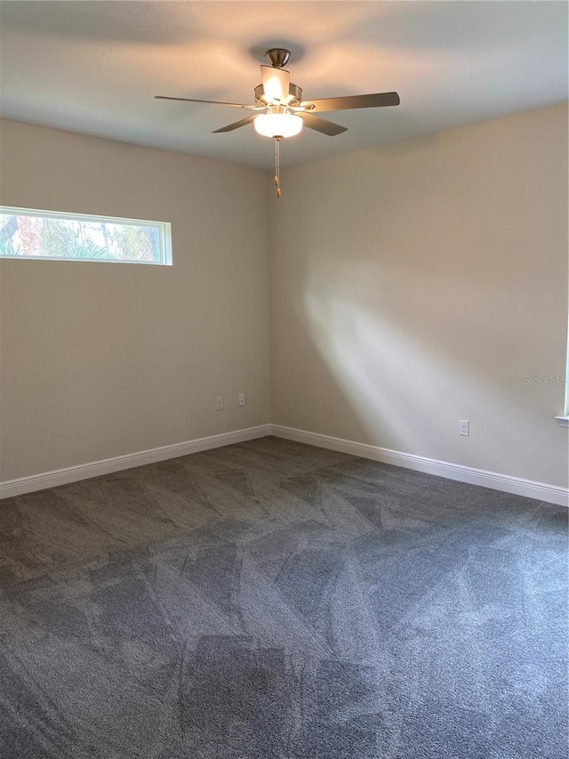 empty room featuring baseboards, dark carpet, and ceiling fan