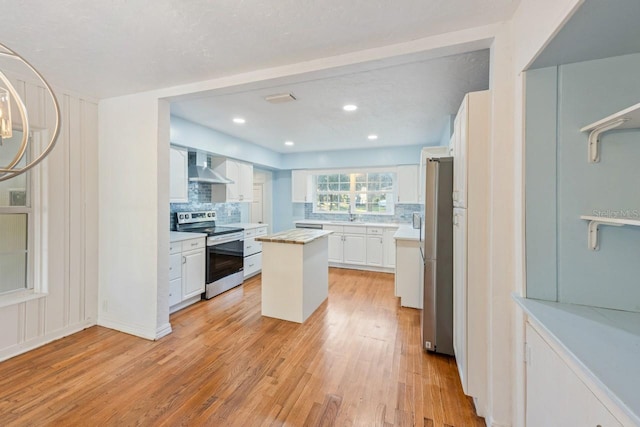 kitchen with appliances with stainless steel finishes, light wood-type flooring, a center island, white cabinetry, and wall chimney range hood