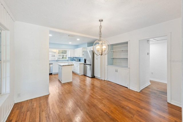 kitchen featuring a center island, decorative light fixtures, decorative backsplash, white cabinetry, and appliances with stainless steel finishes