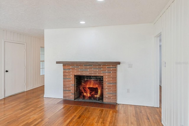 unfurnished living room with a brick fireplace, a textured ceiling, and hardwood / wood-style flooring