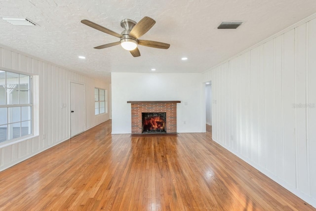 unfurnished living room with a brick fireplace, a textured ceiling, ceiling fan, and light wood-type flooring