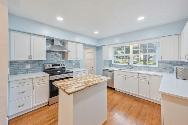 kitchen with wall chimney exhaust hood, white cabinets, a center island, and appliances with stainless steel finishes