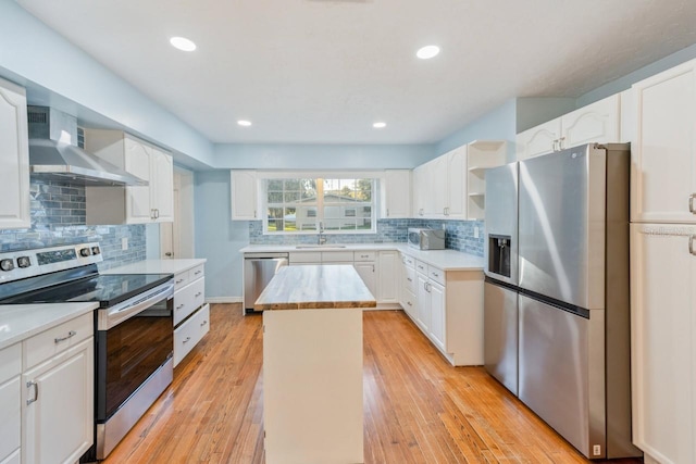 kitchen featuring stainless steel appliances, sink, white cabinetry, a kitchen island, and wall chimney range hood