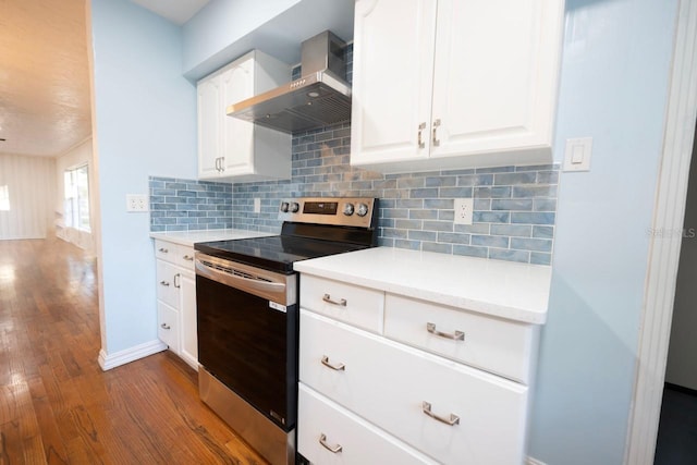 kitchen featuring stainless steel electric range oven, dark hardwood / wood-style flooring, wall chimney exhaust hood, white cabinetry, and backsplash