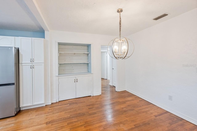 unfurnished dining area with light wood-type flooring, built in shelves, and a notable chandelier