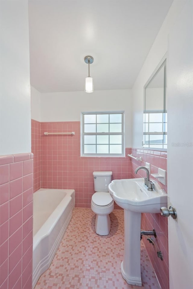 bathroom with tile patterned flooring, toilet, tile walls, a bathing tub, and sink