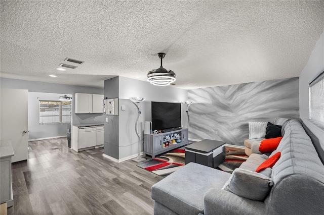 living room with light wood-type flooring, ceiling fan, and a textured ceiling