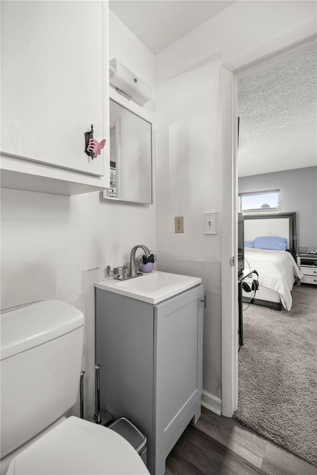 bathroom with a textured ceiling, wood-type flooring, vanity, and toilet