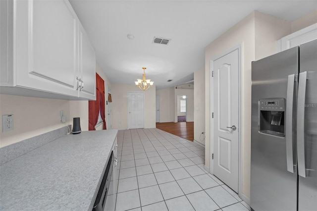 kitchen with a chandelier, light tile patterned floors, stainless steel fridge, white cabinetry, and decorative light fixtures