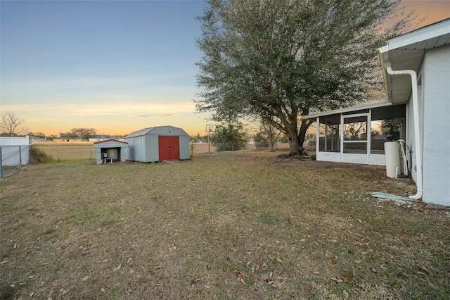 yard at dusk featuring a sunroom and a storage shed