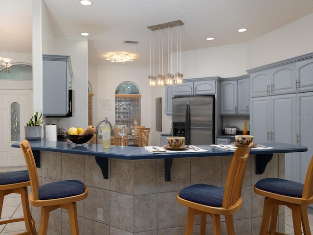 kitchen with kitchen peninsula, pendant lighting, stainless steel fridge, and gray cabinetry