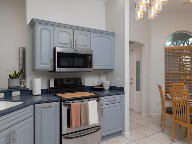 kitchen featuring stainless steel appliances, a notable chandelier, light tile patterned floors, and gray cabinetry