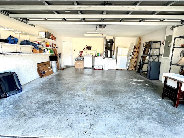 garage featuring heating unit, a garage door opener, washer and dryer, electric panel, and white refrigerator