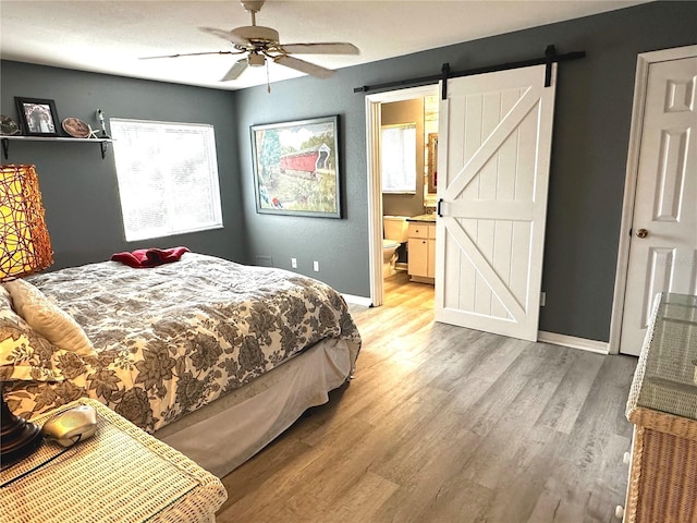 bedroom with ceiling fan, ensuite bath, a barn door, and hardwood / wood-style flooring