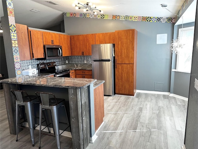 kitchen featuring kitchen peninsula, vaulted ceiling, stainless steel appliances, a breakfast bar, and tasteful backsplash