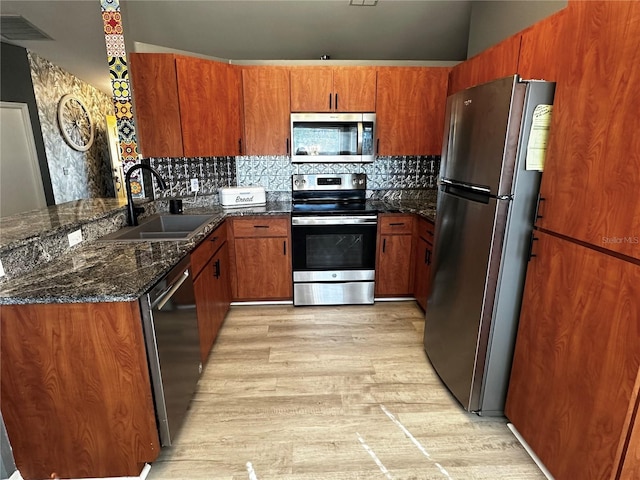 kitchen with light hardwood / wood-style floors, tasteful backsplash, dark stone counters, appliances with stainless steel finishes, and sink