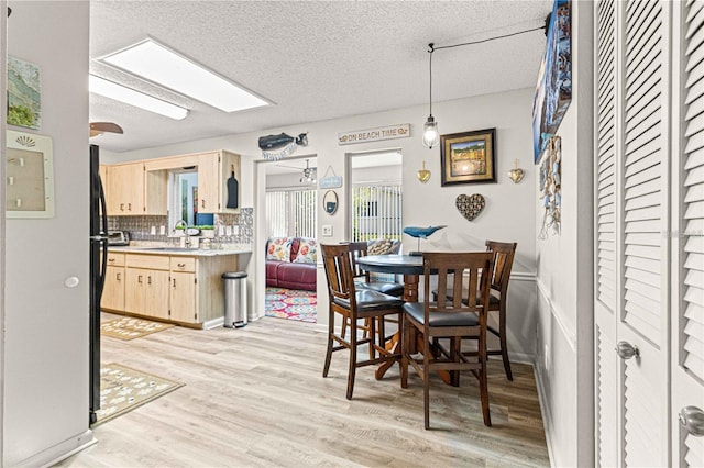 dining area with a textured ceiling, a skylight, light wood-type flooring, and sink