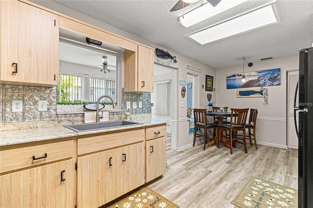 kitchen with a textured ceiling, light brown cabinetry, light hardwood / wood-style floors, and sink