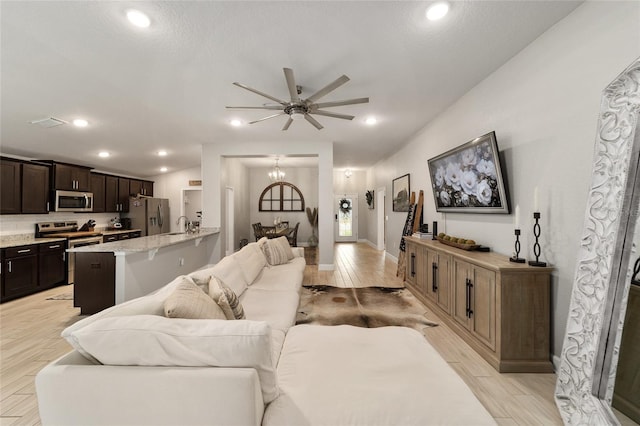 living room featuring ceiling fan with notable chandelier and sink