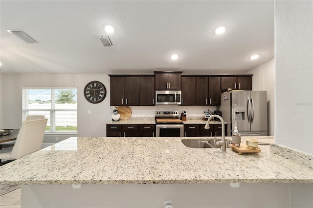 kitchen with sink, stainless steel appliances, dark brown cabinets, and light stone countertops