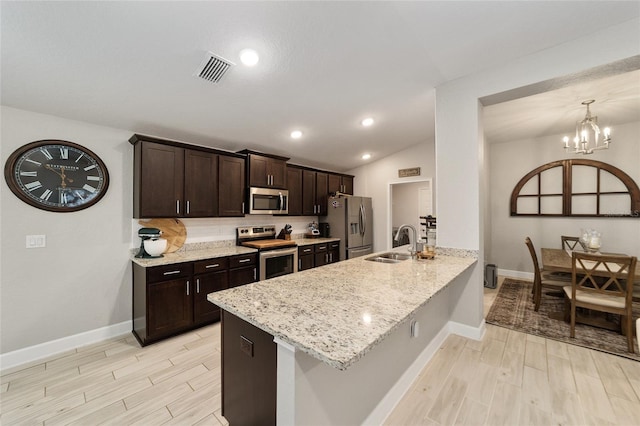 kitchen with sink, light stone counters, kitchen peninsula, a notable chandelier, and appliances with stainless steel finishes