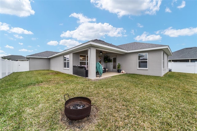 rear view of property featuring a lawn, a patio area, ceiling fan, and a fire pit