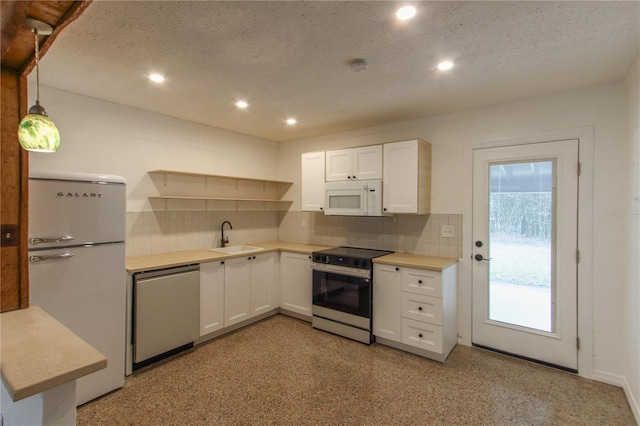 kitchen featuring stainless steel appliances, a textured ceiling, white cabinets, decorative light fixtures, and sink