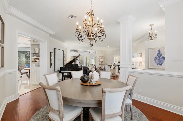 dining room with crown molding, a notable chandelier, hardwood / wood-style floors, and ornate columns