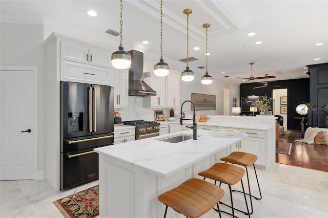 kitchen featuring high end appliances, wall chimney range hood, white cabinetry, and sink