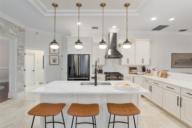 kitchen featuring premium appliances, hanging light fixtures, a kitchen island with sink, light stone countertops, and wall chimney exhaust hood