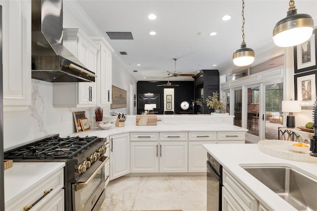 kitchen featuring sink, stainless steel gas range, white cabinetry, decorative light fixtures, and wall chimney exhaust hood