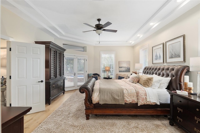 bedroom with light hardwood / wood-style flooring, a raised ceiling, and ceiling fan