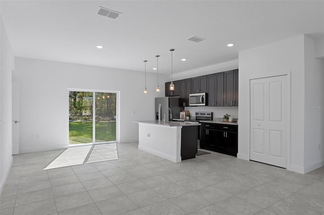 kitchen with light stone countertops, pendant lighting, light tile patterned floors, a kitchen island with sink, and appliances with stainless steel finishes