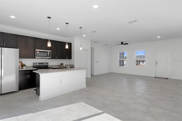 kitchen featuring light stone counters, ceiling fan, pendant lighting, a kitchen island with sink, and appliances with stainless steel finishes