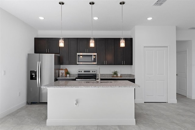 kitchen featuring an island with sink, appliances with stainless steel finishes, light stone countertops, and pendant lighting