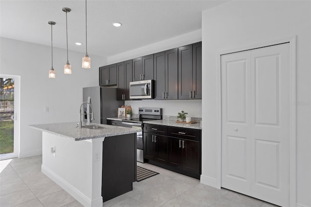 kitchen featuring light tile patterned flooring, an island with sink, light stone countertops, pendant lighting, and appliances with stainless steel finishes