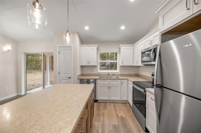 kitchen with stainless steel appliances, sink, decorative light fixtures, white cabinetry, and light hardwood / wood-style floors