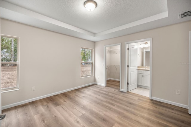 unfurnished bedroom featuring a closet, ensuite bath, a tray ceiling, a textured ceiling, and a walk in closet