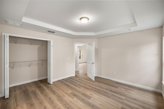 unfurnished bedroom featuring hardwood / wood-style flooring, a closet, a textured ceiling, and a tray ceiling