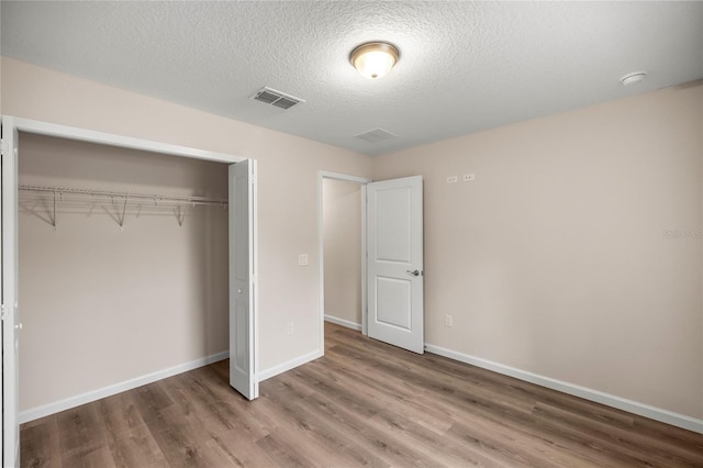 unfurnished bedroom with a textured ceiling, hardwood / wood-style floors, and a closet