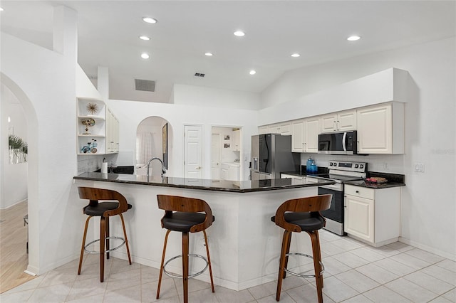 kitchen featuring stainless steel appliances, dark stone countertops, tasteful backsplash, kitchen peninsula, and a breakfast bar area