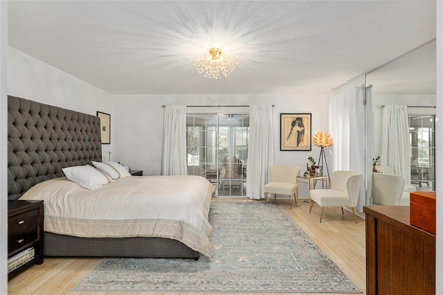 bedroom featuring a textured ceiling, an inviting chandelier, access to outside, and light hardwood / wood-style flooring