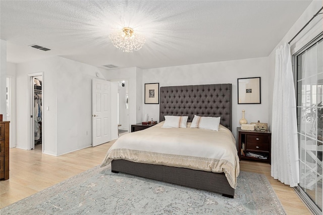 bedroom with a walk in closet, light wood-type flooring, a closet, and a textured ceiling