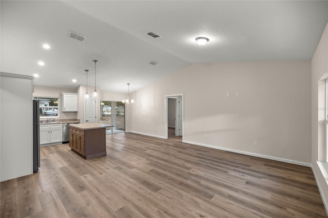 kitchen featuring white cabinets, vaulted ceiling, black refrigerator, hanging light fixtures, and a kitchen island