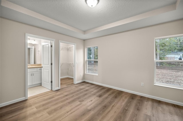 unfurnished bedroom featuring a closet, a walk in closet, ensuite bathroom, and multiple windows